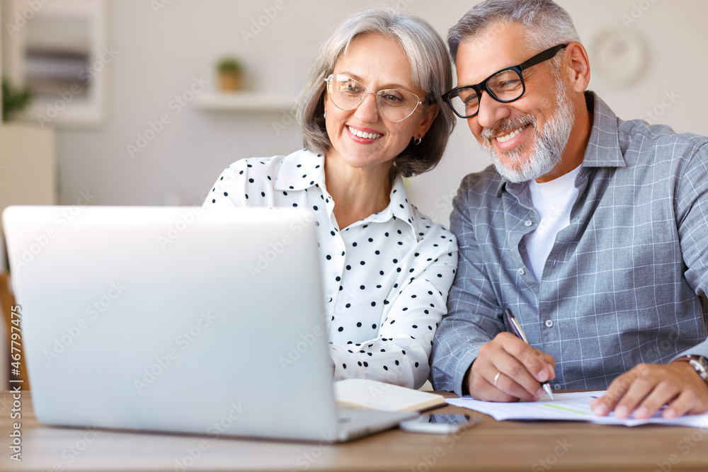 Senior happy family couple doing homework together while studying online on laptop at home Senior happy family couple doing homework together while studying online on laptop at home