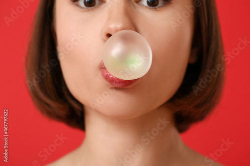 Young woman with chewing gum on color background, closeup