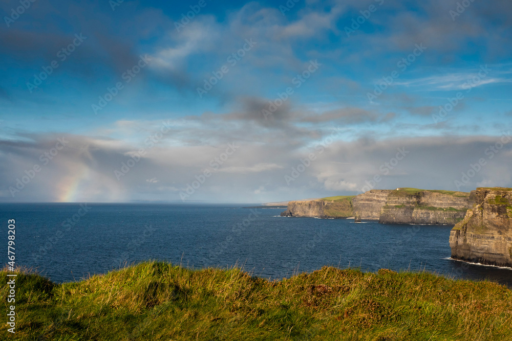 Obraz premium Colorful rainbow in the ocean next to Cliff of Moher, county Clare, Ireland. Amazing scenery with great view. Cloudy sky and blue ocean water. Top Irish nature landmark and travel destination