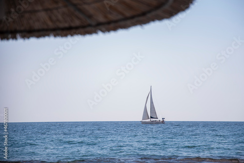 Reed umbrella. Beautiful modern sailboat sailing blue Aegean sea.Luxury boats. Summer adventure, active vacation in Nea Skioni, Greece.