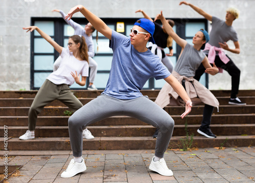 Positive teen boy dancing modern street dance outdoors with teenagers in background. photo