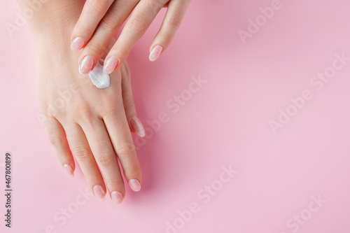 A young woman is applying cream to her hands. Spa and body care concept on a pink background. Image for advertising.