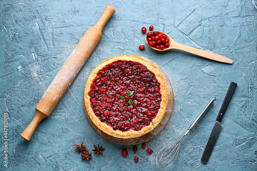 Foto Board with tasty lingonberry pie and kitchen utensils on color background