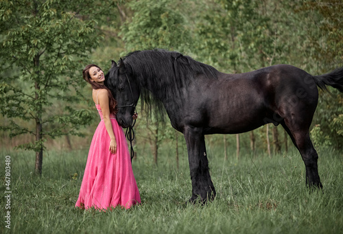 Beautiful long-haired girl in a dress next to a black horse