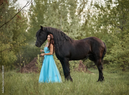 Beautiful long-haired girl in a dress next to a black horse