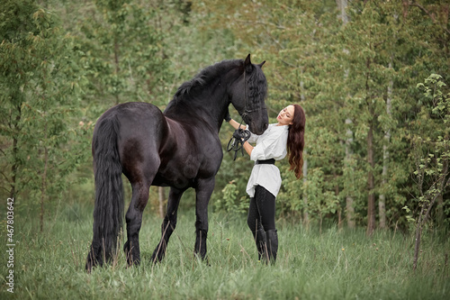 Beautiful long-haired girl with a Friesian horse