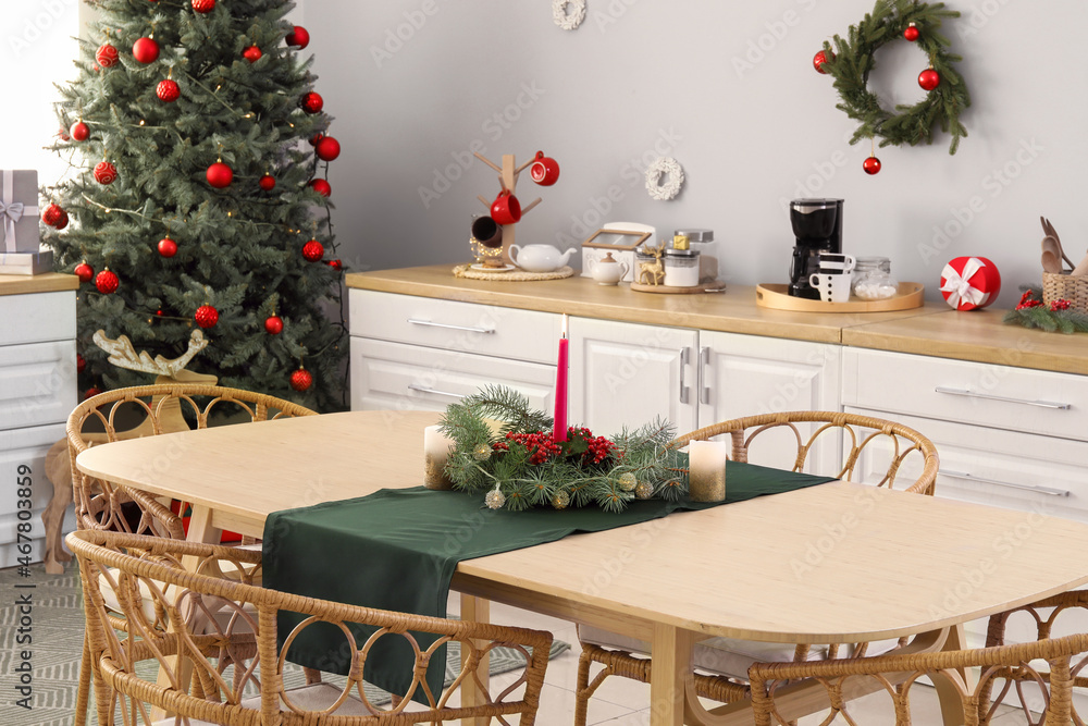 Dining table with burning candle and fir branches in kitchen decorated for Christmas