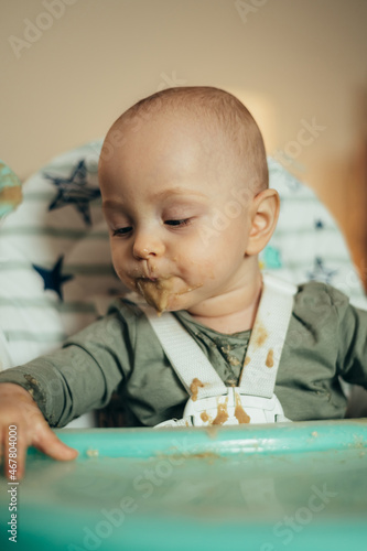 Baby eating with a face stained in food while in a child's dining chair