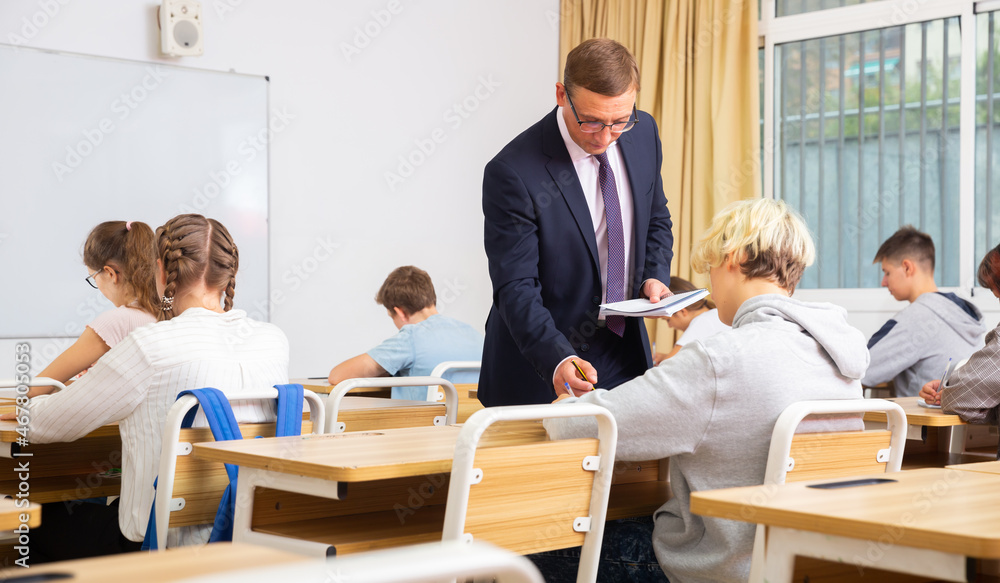 Positive teacher helping teenage schoolchildren during lesson in schoolroom