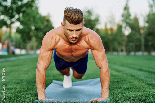 athletic man with pumped up muscular body in the park doing exercise