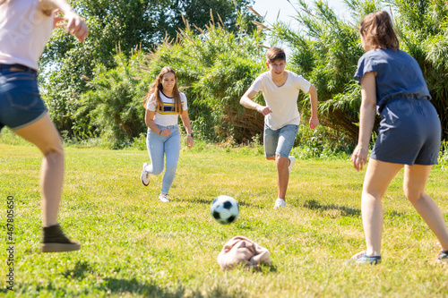Cheerful teen friends gaily spending time together on summer day, playing with ball outdoors
