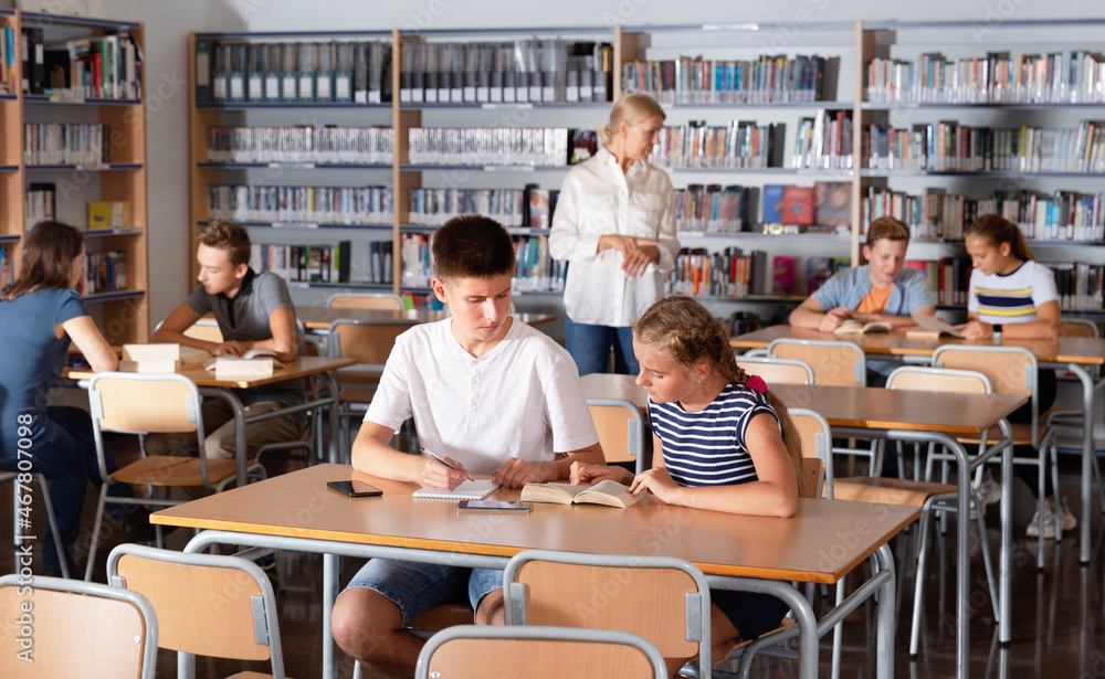 Obraz premium Diligent efficient glad schoolchildren preparing for lesson in school library, reading and writing