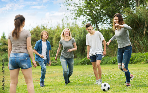 Three happy girls and two positive boys teenagers friends running with ball on meadow outdoors