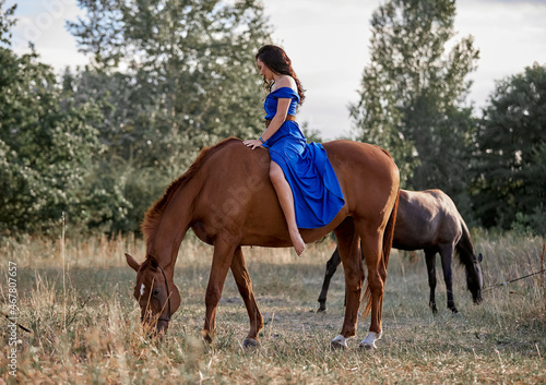 Beautiful long-haired girl in a blue dress riding a red horse