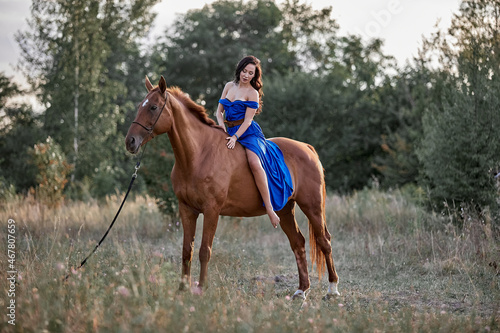 Beautiful long-haired girl in a blue dress riding a red horse