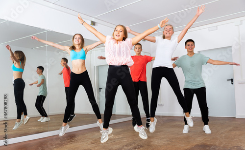 Group of happy teens jumping with female coach during exercising in choreography class ..