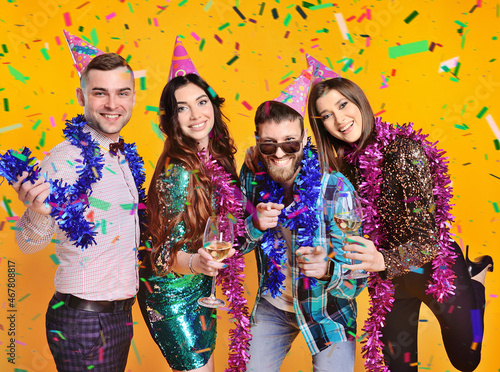 a group of friends in birthday caps and tinsel celebrate a birthday or New Year's party on a confetti and yellow background