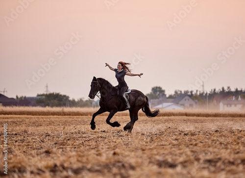 Girl riding a friesian horse in a field at sunset