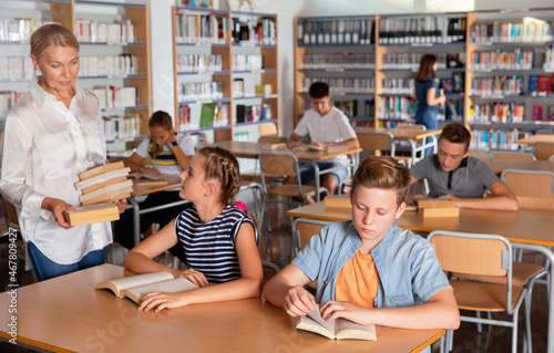 Upset efficient serious boy and girl sitting with books during lesson, teacher helping them in classroom