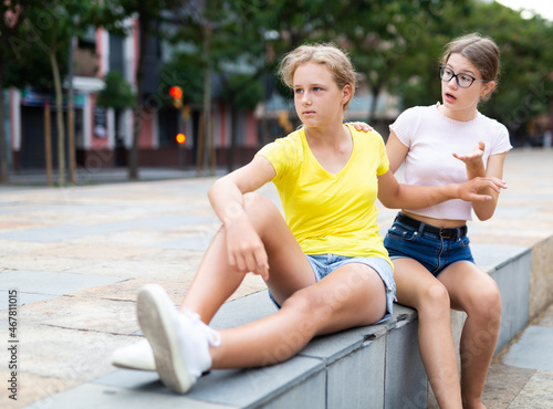 Two teenager girls quarreling while sitting in urban park.