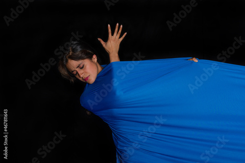 Latin woman with indigenous features with her body wrapped in a blue cloth with an expression of pain on her face on a black background