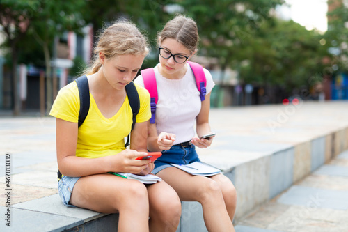 Teen girls teach lessons using smartphones outdoors near college