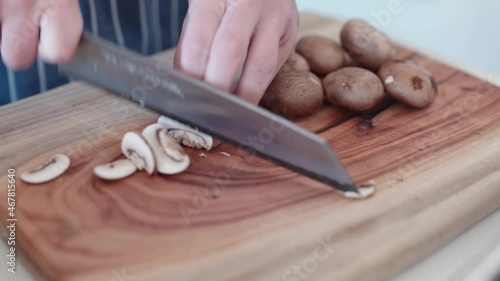 Close up of chef finely slicing swiss mushrooms on a wooden cutting board. 