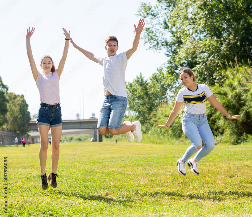 Cheerful teen friends gaily spending time together on summer day, jumping together in city park..