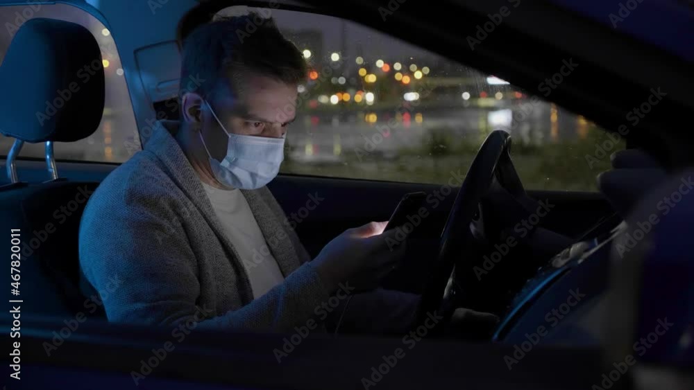Delivery service man wearing his protective mask due to Covid-19 late nigt with a delivery item in a car. Volunteer Work in the Midst of an Epidemic. Courier with a Cardboard Box Package on a second Delivery service man wearing his protective mask due to Covid-19 late nigt with a delivery item in a car. Volunteer Work in the Midst of an Epidemic. Courier with a Cardboard Box Package on a second