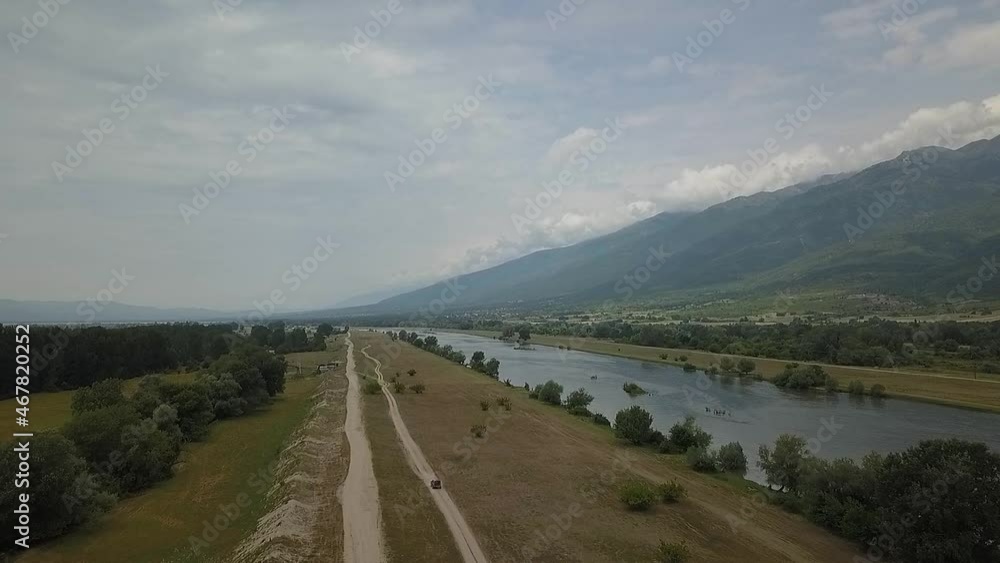High aerial shot from a drone following a Landrover Freelander 2 driving off-road down a dirt track along a river with mountains in the background. High aerial shot from a drone following a Landrover Freelander 2 driving off-road down a dirt track along a river with mountains in the background.