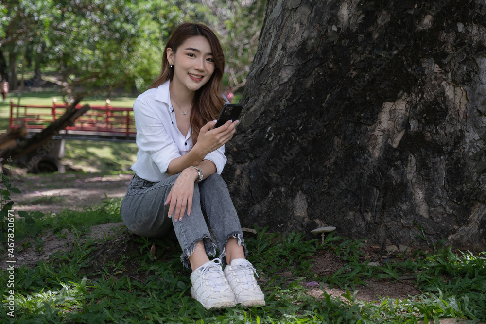 Image of pleased positive woman sitting outdoors in park and using cell phone Image of pleased positive woman sitting outdoors in park and using cell phone