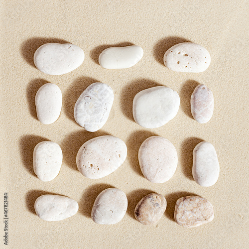Pattern with white pebble sea stones on fine sand. Square composition from natural stone neutral beige color, monochrome tones. Spa minimal background