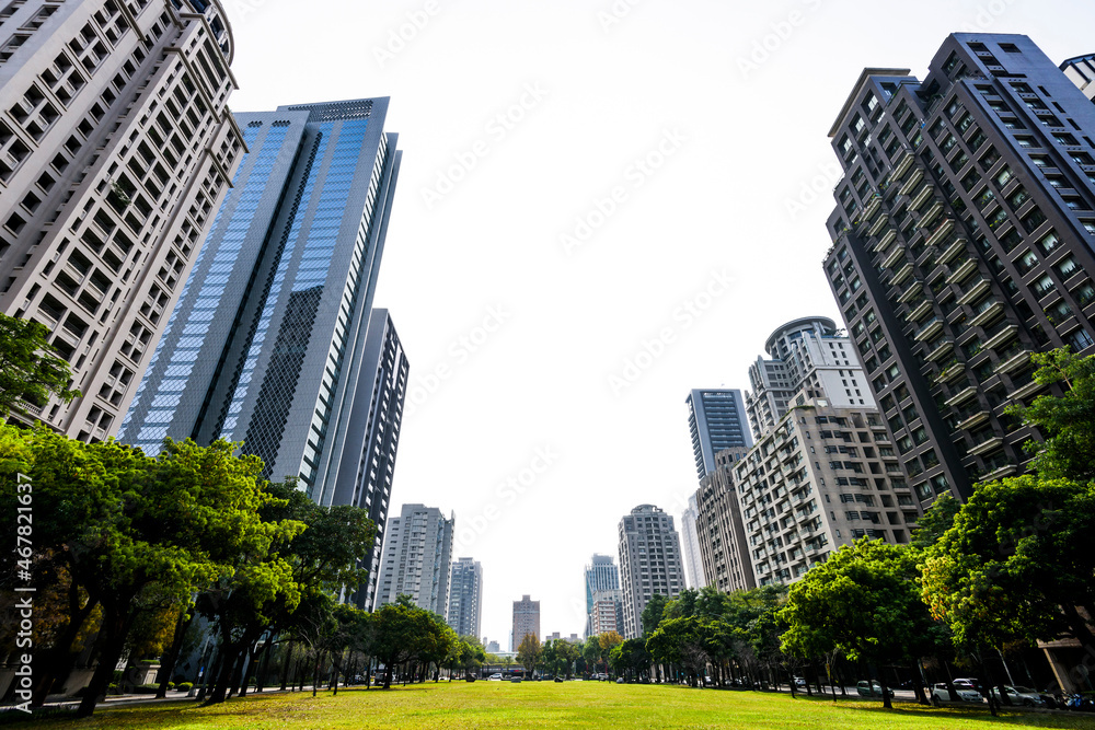 Obraz premium Low-angle view of green park space and modern buildings on both sides in downtown Taichung, Taiwan. here is near the National Taichung Theater.
