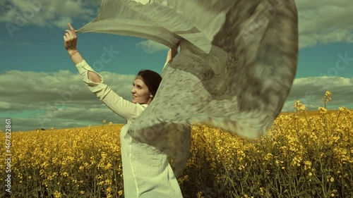 Beautiful woman with wind fluttering scarf in the rapeseed field. Woman freedom. Women rights.