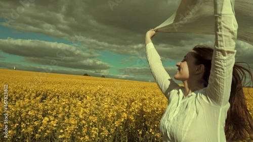 Beautiful woman with wind fluttering scarf in the rapeseed field. Woman freedom. Women rights.