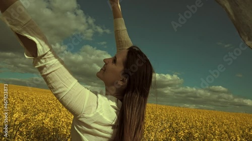 Beautiful woman with wind fluttering scarf in the rapeseed field. Woman freedom. Women rights.
