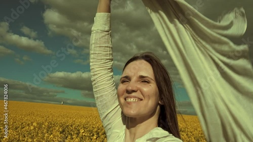 Beautiful woman with wind fluttering scarf in the rapeseed field. Woman freedom. Women rights.