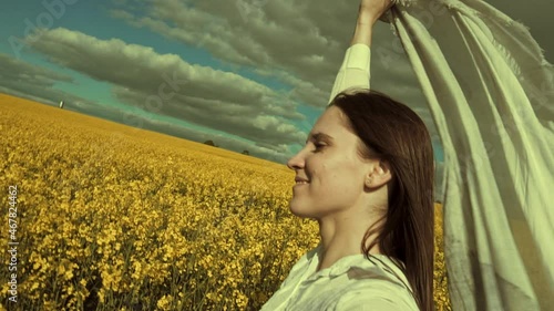 Beautiful woman with wind fluttering scarf in the rapeseed field. Woman freedom. Women rights.