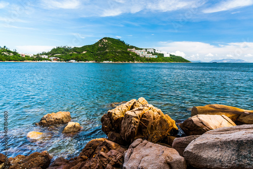The rocky seashore of Stanley Bay on Hong Kong Island in Hong Kong. Beautiful scenic landscape with water, mountains, rocks, buildings, fishing boats, and cloudy sky.