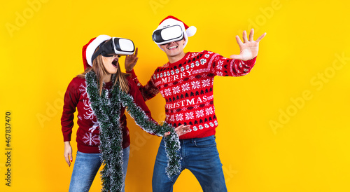 young latin couple gamer in virtual reality headset gadget wearing Santa hat and Christmas sweater on yellow background. Christmas and winter vr technology concept in Mexico Latin America