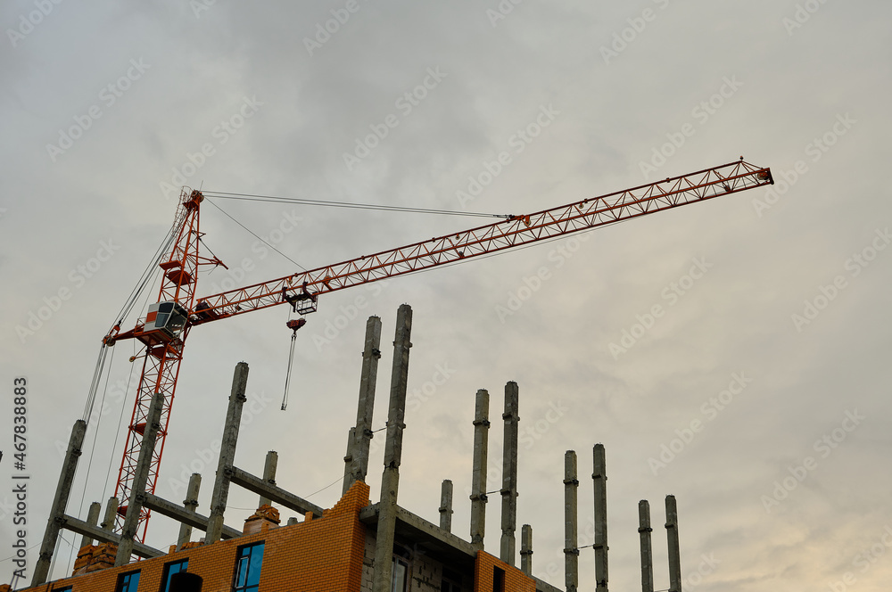 High rise construction crane on background of an unfinished multi storey and multi apartment residential building. High rise construction crane on background of an unfinished multi storey and multi apartment residential building.