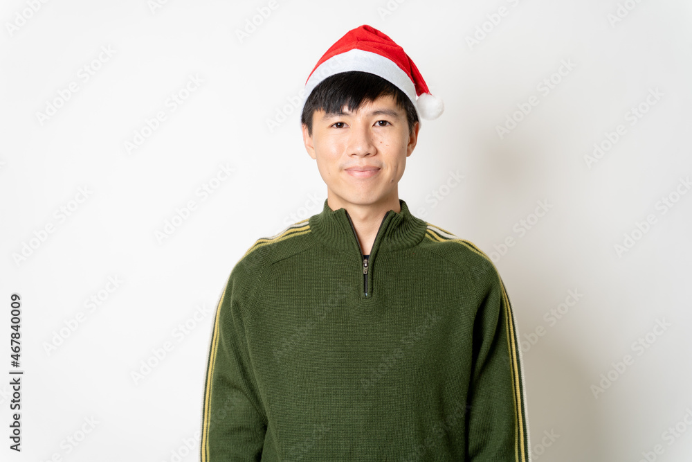 Portrait of happy young adult Asian handsome man with green sweater, Christmas hat or Santa's hat on empty copy space for texting or advertisement on isolated white background. Asian Christmas concept Portrait of happy young adult Asian handsome man with green sweater, Christmas hat or Santa's hat on empty copy space for texting or advertisement on isolated white background. Asian Christmas concept