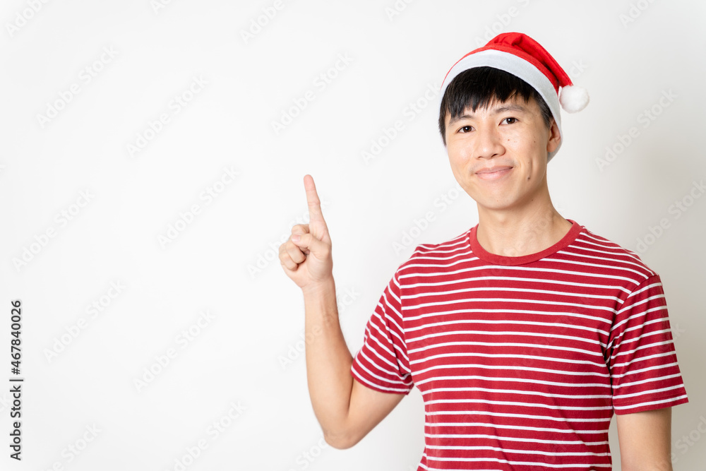 Happy young adult Asian man with Christmas theme t-shirt, Christmas hat or Santa's hat pointing on empty copy space for texting or advertisement on isolated white background. Asian Christmas concept. Happy young adult Asian man with Christmas theme t-shirt, Christmas hat or Santa's hat pointing on empty copy space for texting or advertisement on isolated white background. Asian Christmas concept.