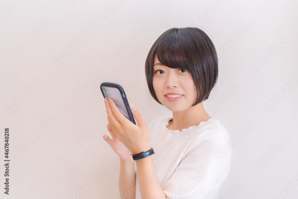 スマホを持ちながらこちらを見て笑う女性 スマホを持ちながらこちらを見て笑う女性