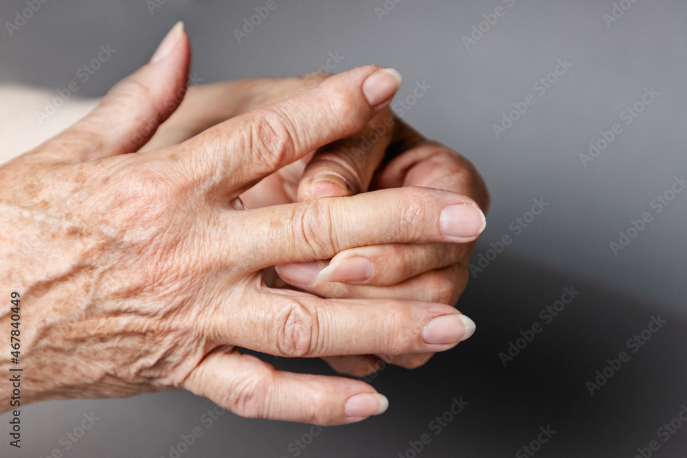 A senior woman massages her fingers, experiencing pain in the joints. Gray background, hands close-up. The concept of rheumatism and arthritis A senior woman massages her fingers, experiencing pain in the joints. Gray background, hands close-up. The concept of rheumatism and arthritis