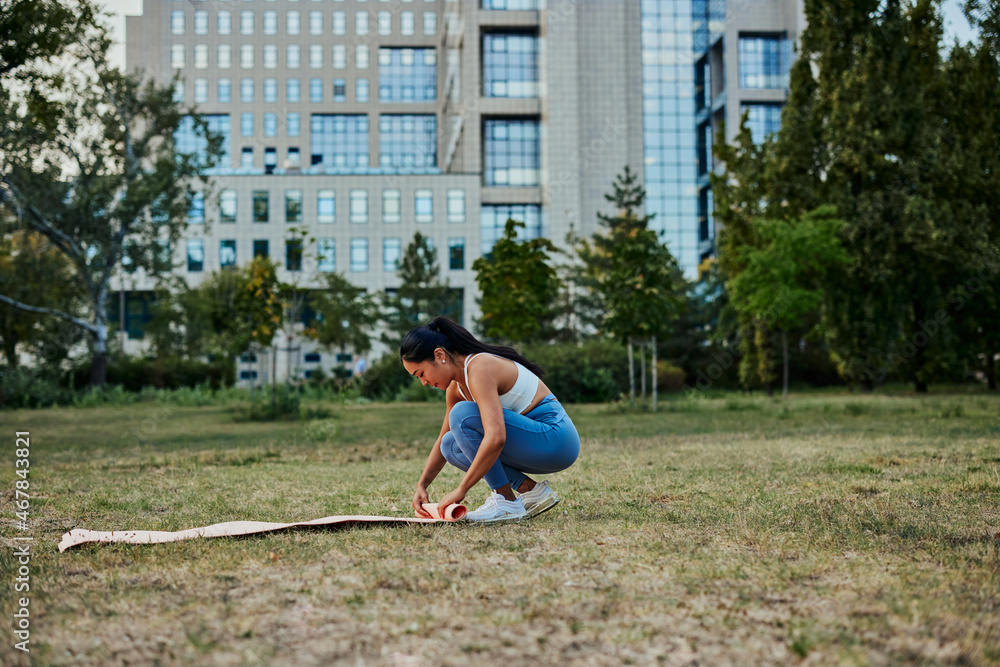 Fototapeta premium Asian woman unrolling yoga mat for doing yoga in park