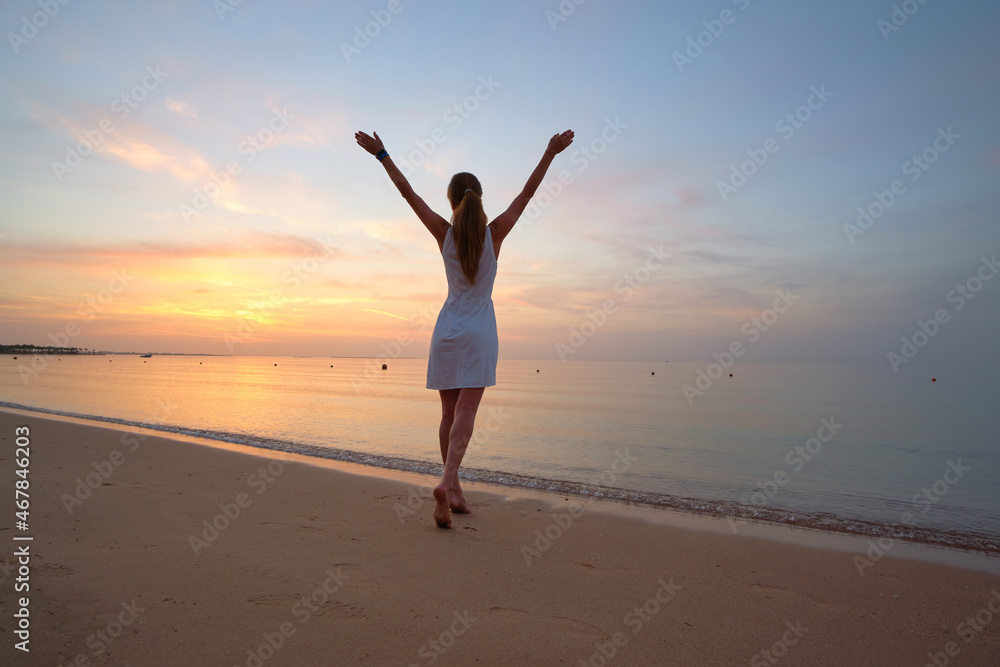 Young happy woman standing on sandy beach by seaside enjoying warm tropical evening Young happy woman standing on sandy beach by seaside enjoying warm tropical evening