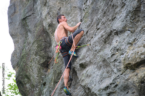Young man climbing steep wall of rocky mountain. Male climber overcomes challenging route. Engaging in extreme sport concept