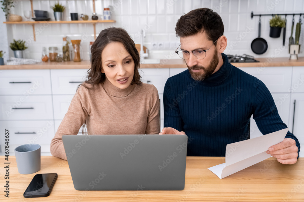 Family couple making the utility bills sitting at home kitchen using laptop Family couple making the utility bills sitting at home kitchen using laptop