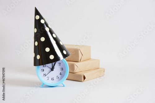 blue alarm clock in party hat and goft boxes on gray background concept party time